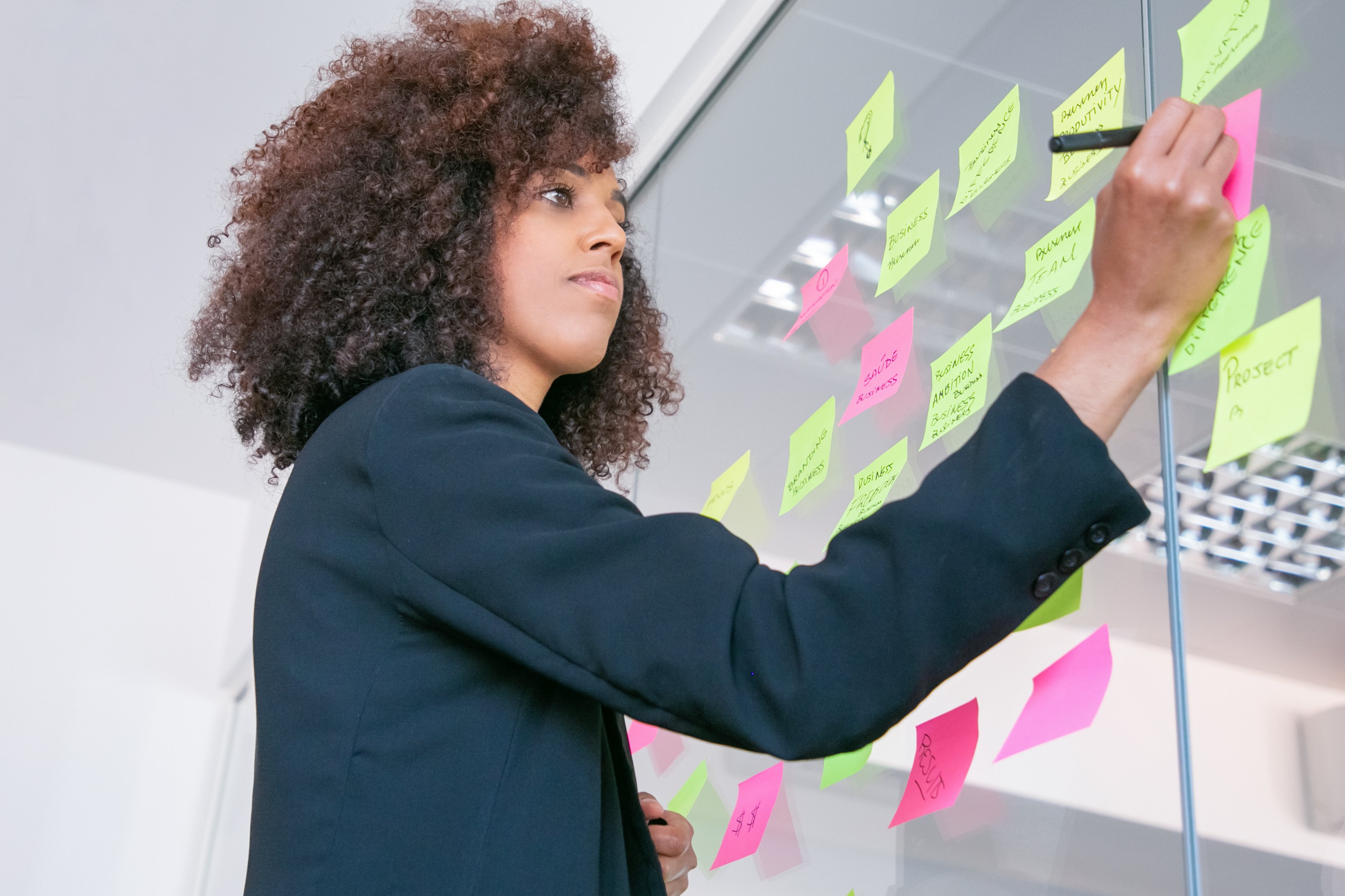successful-pretty-businesswoman-writing-on-sticker-with-marker-thoughtful-confident-curly-female-manager-sharing-idea-for-project-and-making-note-brainstorming-business-and-training-c